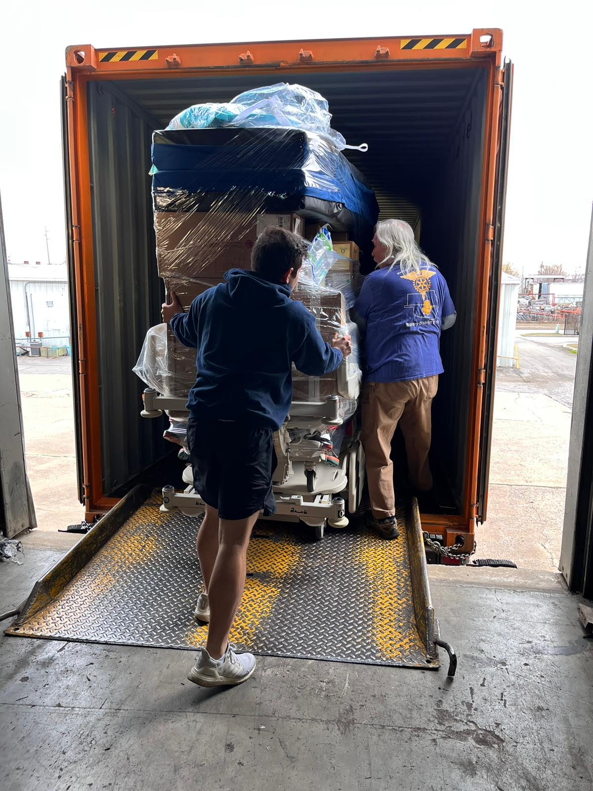 Volunteers loading a wrapped pallet of donated hospital equipment into a shipping container